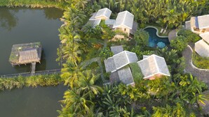 An aerial view of a resort with multiple bungalow-style buildings, a swimming pool, and lush tropical vegetation. - An Villa Hoi An (Da Nang)