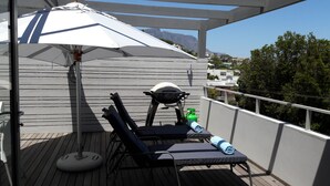 Un balcon équipé de deux fauteuils de jardin, d’un barbecue et d’un parasol.