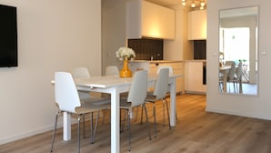 Une cuisine moderne avec des meubles blancs, une table à manger avec des chaises et un vase rempli de fleurs.