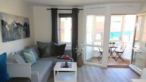 Un salon moderne avec un canapé gris, une table basse blanche et une grande fenêtre avec des rideaux.