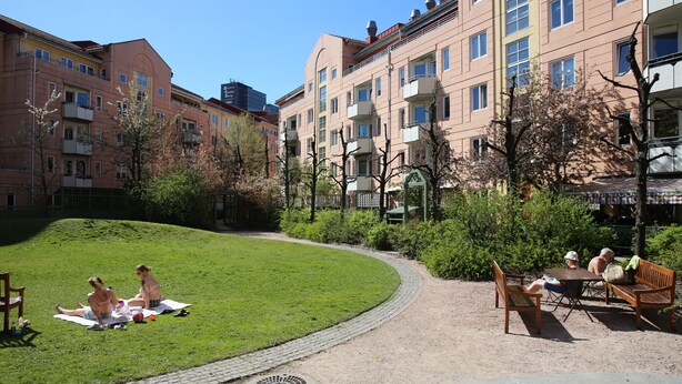 Une cour comprenant un espace gazonné, un chemin pavé et un coin salon avec des bancs et des tables.