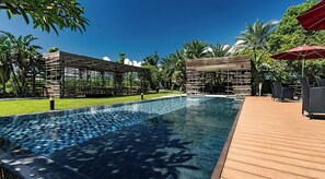 A pool area with a wooden deck, lounge chairs, and umbrellas.