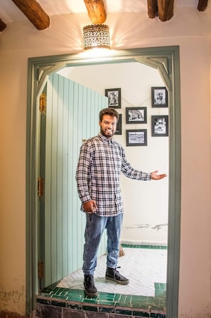 Un hombre de pie en un umbral, con techo de madera y una lámpara colgante.