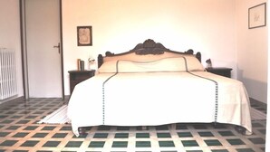 Uma cama com colcha branca e cabeceira decorativa em um quarto com piso xadrez.