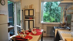 Uma cozinha compacta com uma mesa de jantar para dois, um armário embutido com potes de temperos, uma janela com vista para o verde e um fogão branco.