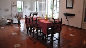 Uma área de refeições com toalha xadrez vermelha, cadeiras de madeira e chão ladrilhado.