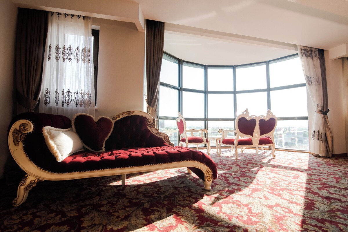 A room with a red velvet sofa, matching chairs, and a large window with a view.