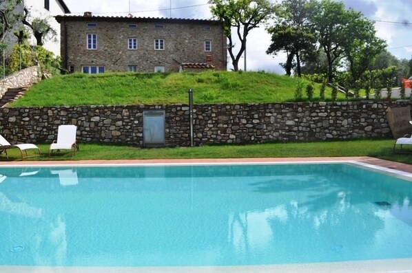 Ein Steinhaus mit Swimmingpool, weißen Liegestühlen und einer Steinmauer.