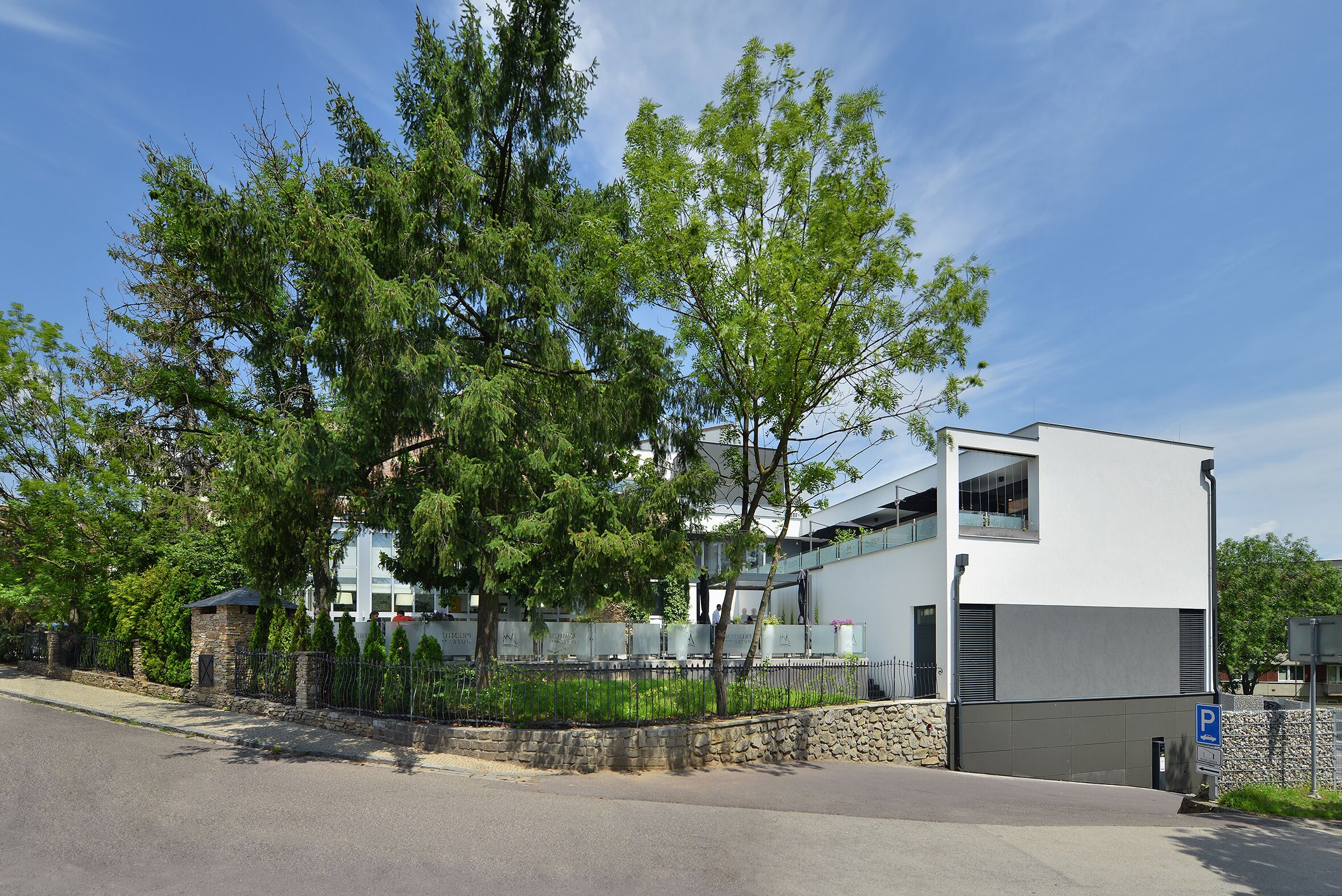 A modern building with a glass facade, a stone wall, and a parking sign.