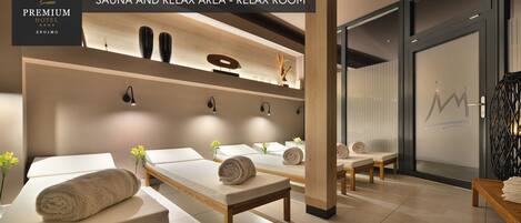 Un cuarto de spa con varias camillas de masaje, cada una con una toalla y una pequeña planta. Hay luces fijadas en la pared y un estante decorativo sobre las camillas.