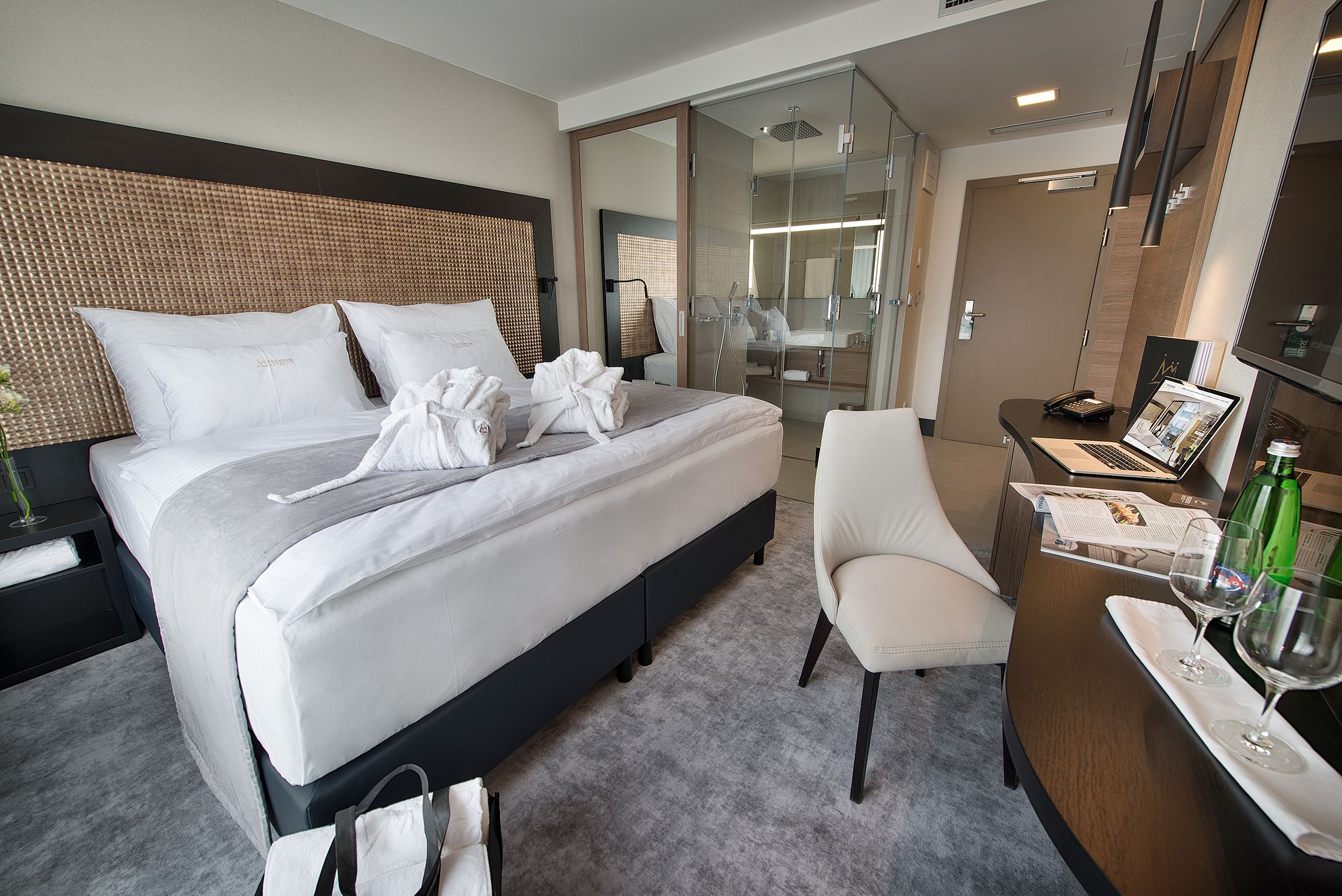 A hotel room with a large bed, a desk with a laptop, a chair, and a bathroom visible through an open door.