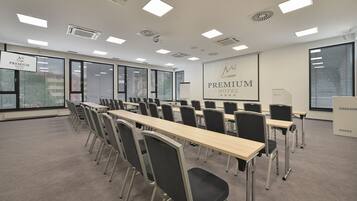 A conference room with long tables and chairs, large windows with blinds, and a projection screen displaying "PREMIUM HOTEL".