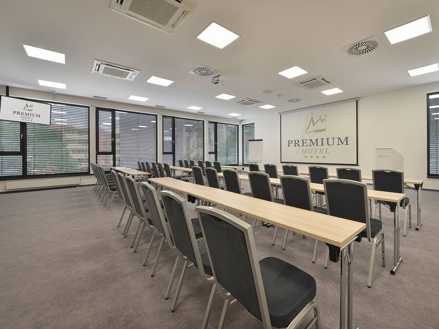 A conference room with long tables and chairs, large windows with blinds, and a projection screen displaying "PREMIUM HOTEL".