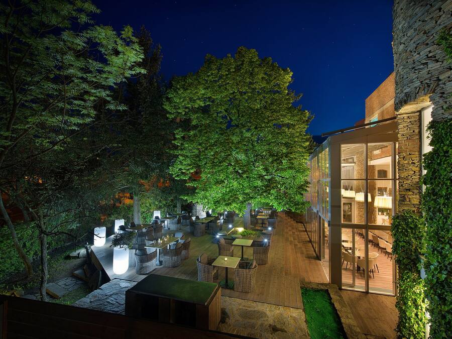 Un espace de restauration en plein air, avec des tables et des chaises, entouré d’arbres et bordé d’un bâtiment en pierre.