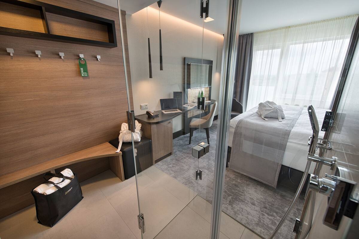 A modern hotel room with a bed, desk, chair, and a glass partition.