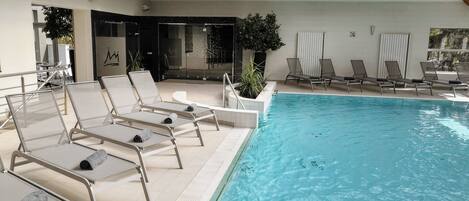 Una piscina interior con sillones de descanso y una estructura de techo de madera.