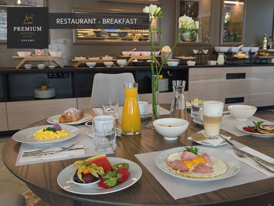 Une table de petit-déjeuner dressée dans un hôtel, avec une variété de plats proposés, notamment des œufs, des viennoiseries et des fruits, et une cuisine moderne en arrière-plan.