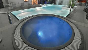 A large indoor swimming pool with a hot tub, surrounded by lounge chairs and a seating area.