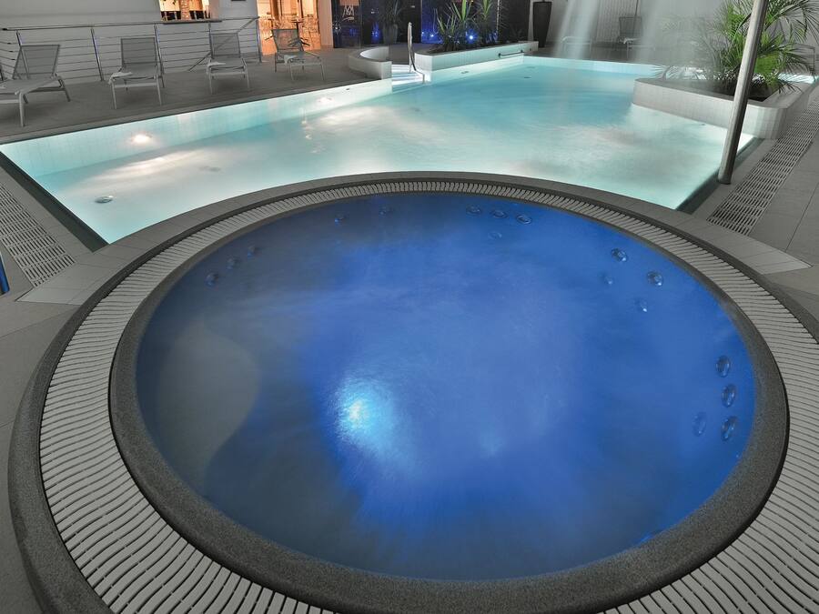 A large indoor swimming pool with a hot tub, surrounded by lounge chairs and a seating area.