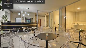 A modern wellness bar and massage area with clear chairs and tables, a reception desk, and a minibar.