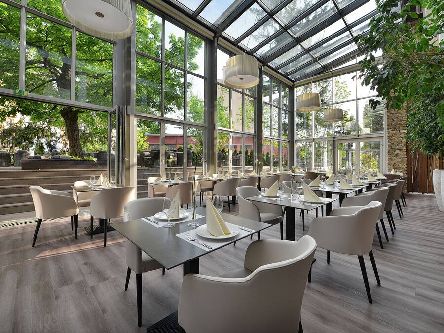 A restaurant with a glass ceiling, wooden flooring, and white chairs.