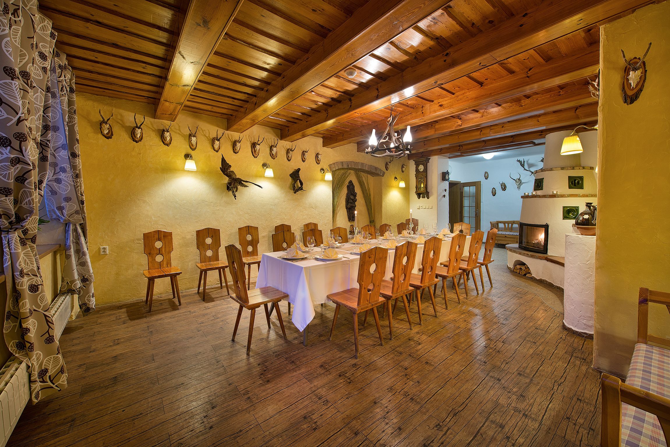 Un comedor con sillas y mesas de madera, un candelabro y cabezas de animales colgadas en la pared.