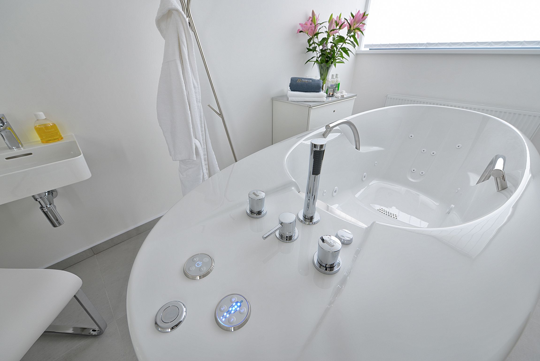 Un baño moderno con una bañera independiente, un lavabo blanco y una pequeña cómoda.