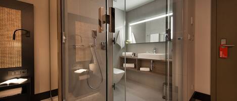 A modern bathroom with a glass-enclosed shower, a toilet, and a sink with a mirror above it.