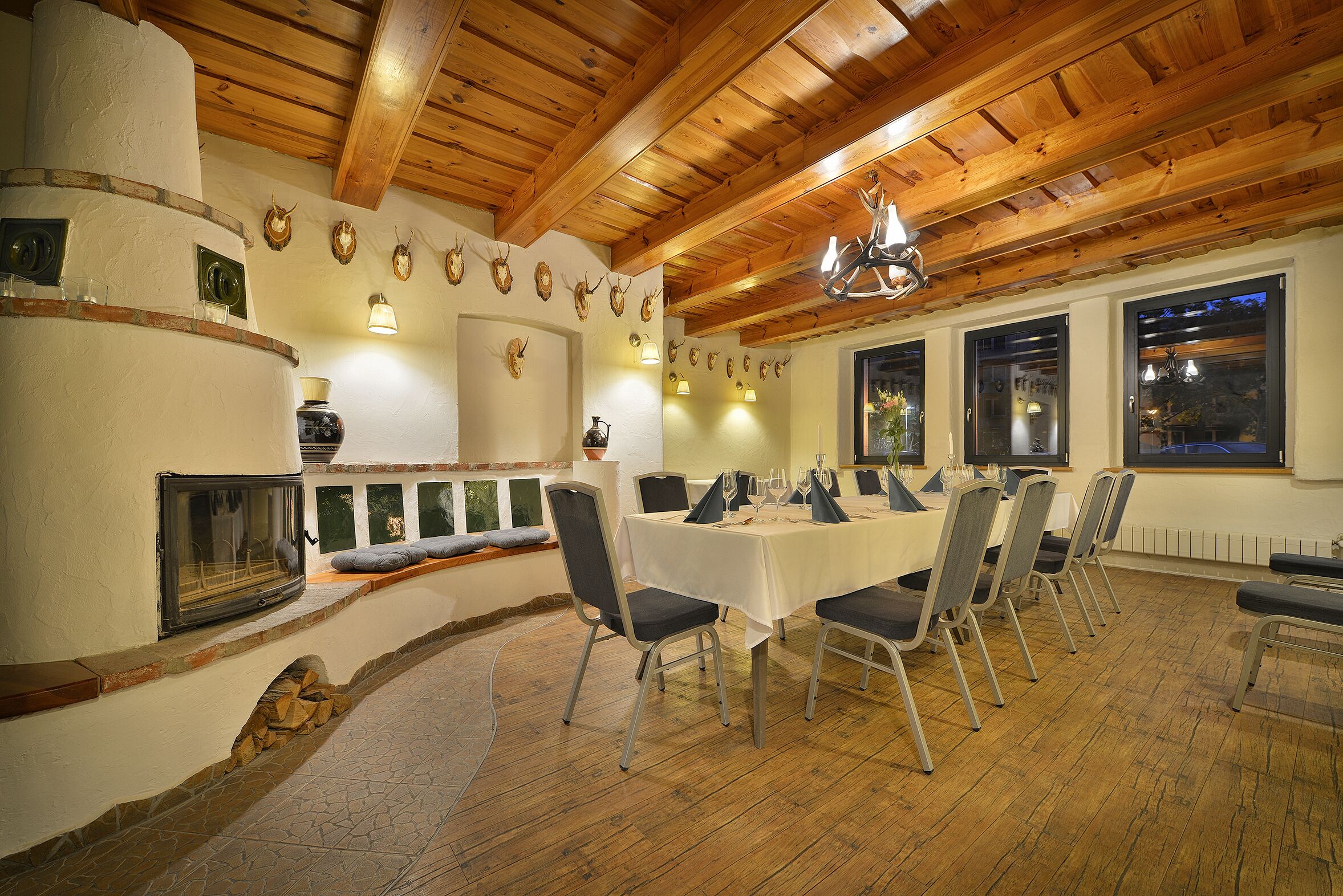 A dining area with a long table set for a meal, wooden ceiling beams, and mounted animal heads on the wall.