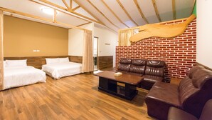 A room with two beds, a leather sofa, a wooden coffee table, and a brick wall.