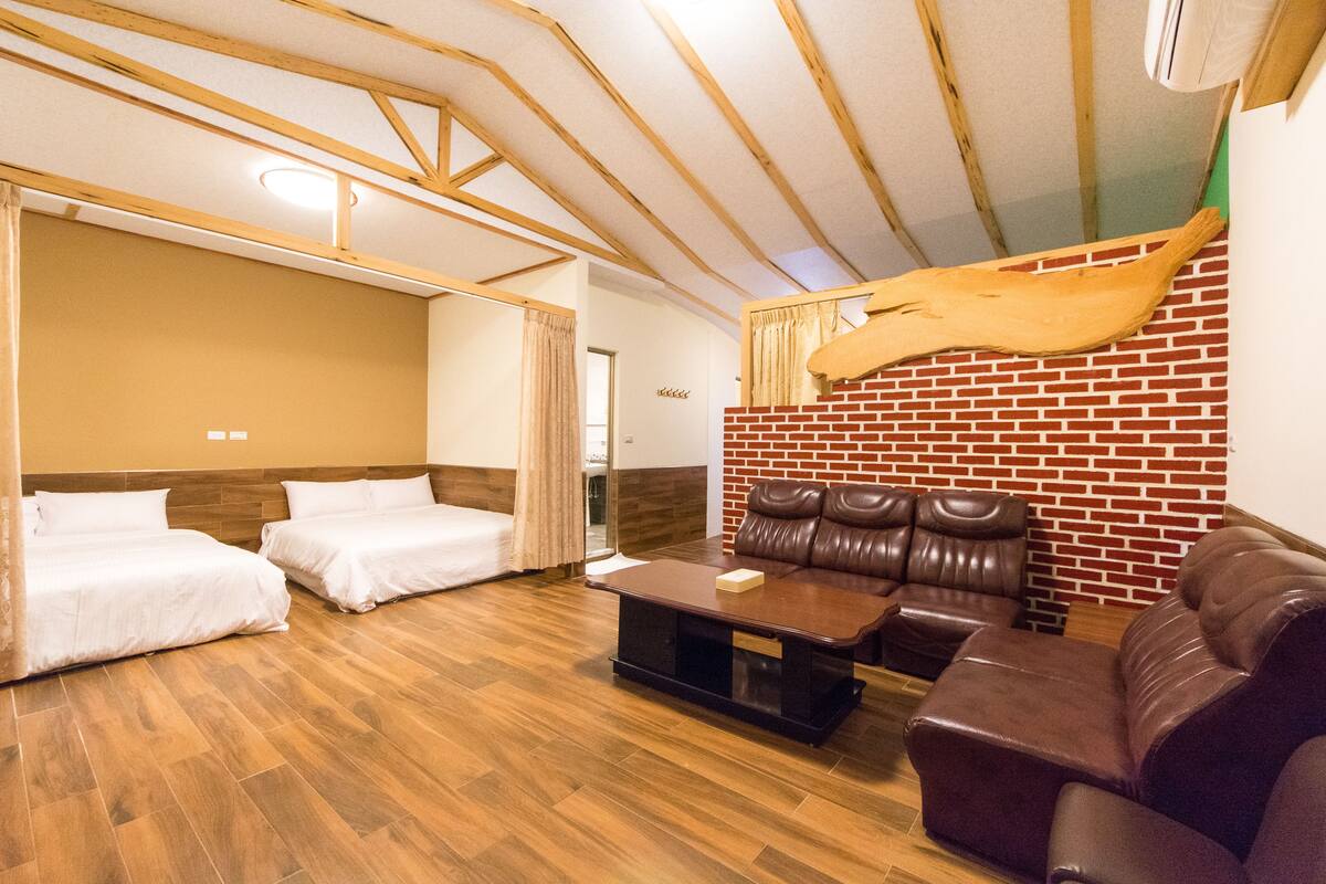 Una habitación con dos camas, un sofá de cuero, una mesa de centro de madera y una pared de ladrillo.