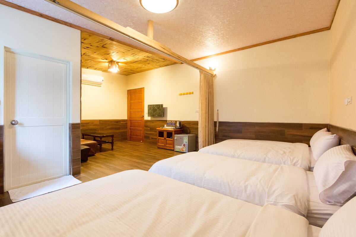 Habitación de hotel con dos camas, techo de madera, una kitchenette pequeña y un banco de madera.