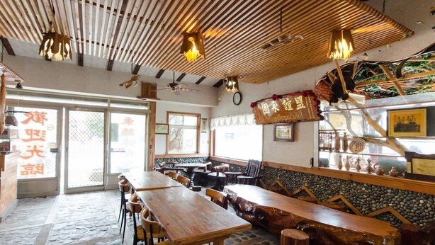 A restaurant interior with wooden tables and benches, a stone floor, and a bamboo ceiling.