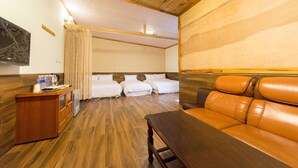 A hotel room with a wooden ceiling, a TV, a desk with a computer, a sofa, and three beds.