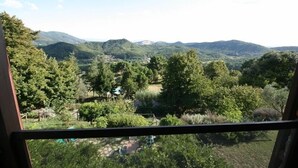 Vista da janela com paisagem montanhosa, vegetação densa e céu claro.