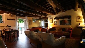 Uma sala de estar acolhedora com um sofá, uma mesa de jantar com cadeiras e uma cozinha visível através de uma porta aberta.