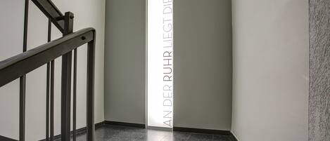 A hallway with a metal staircase on the left and a vertical sign with text.