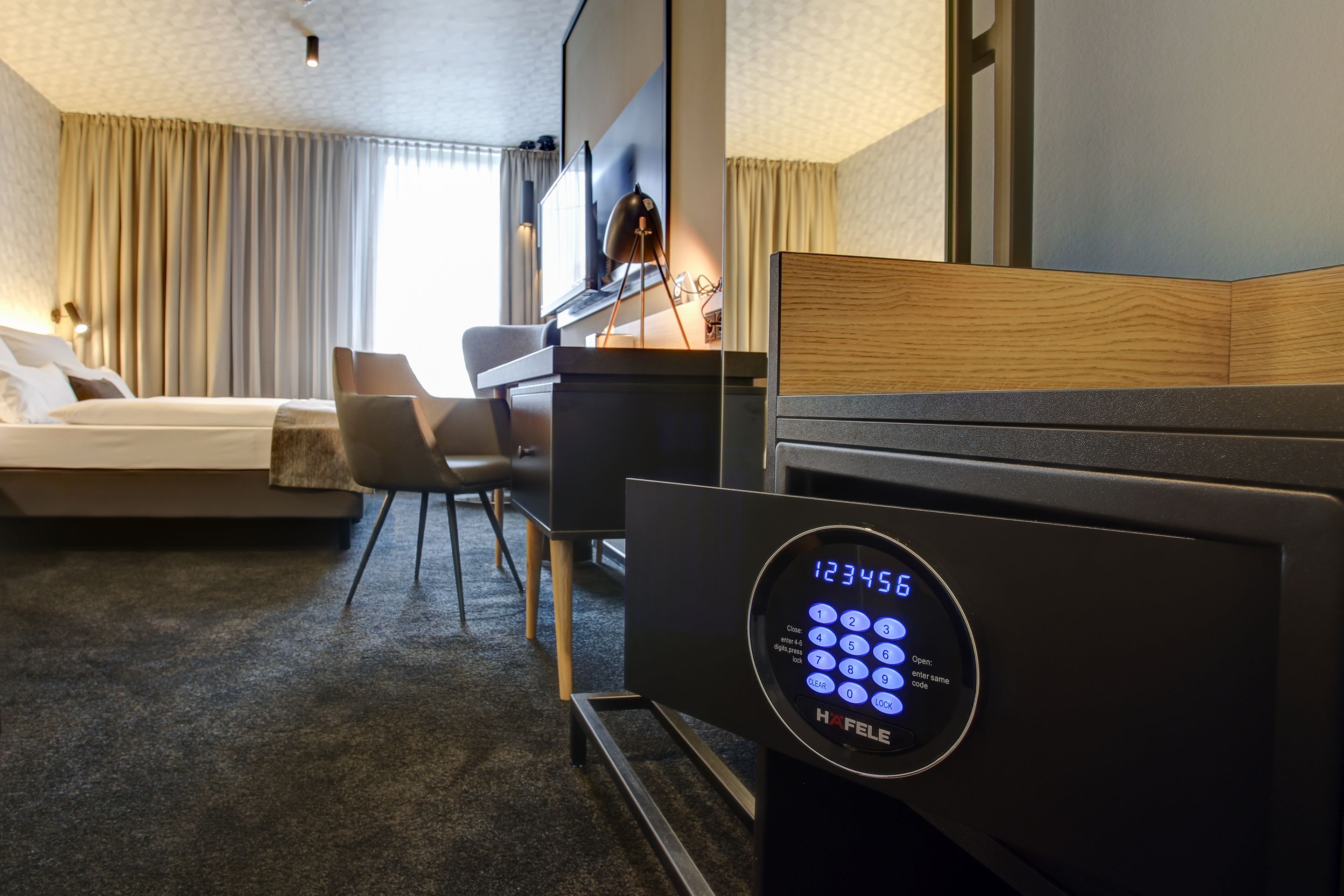 Une chambre d’hôtel équipée d’un lit, d’un bureau, d’une chaise et d’un panneau de contrôle numérique pour la serrure.