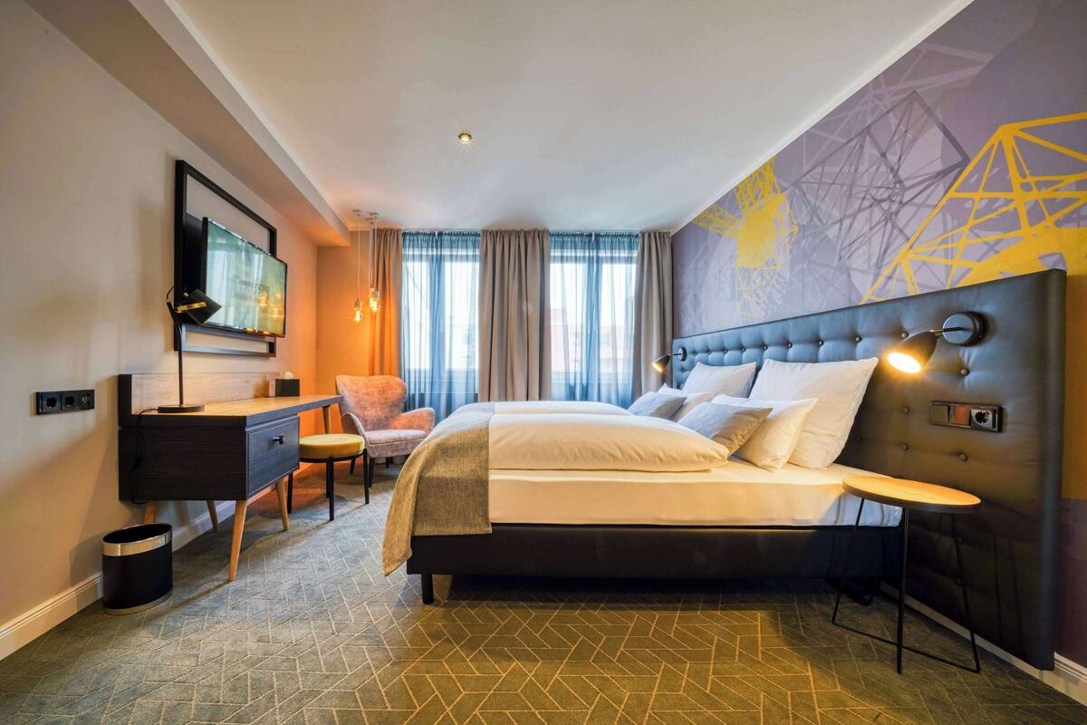 Une chambre d’hôtel moderne, dotée d’un grand lit, d’un bureau, d’une chaise et d’un téléviseur fixé au mur.