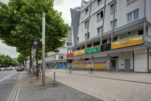 Ein mehrstöckiges Gebäude mit einem Supermarkt im Erdgeschoss, einem Fahrradstellplatz und einem Fußgängerweg.