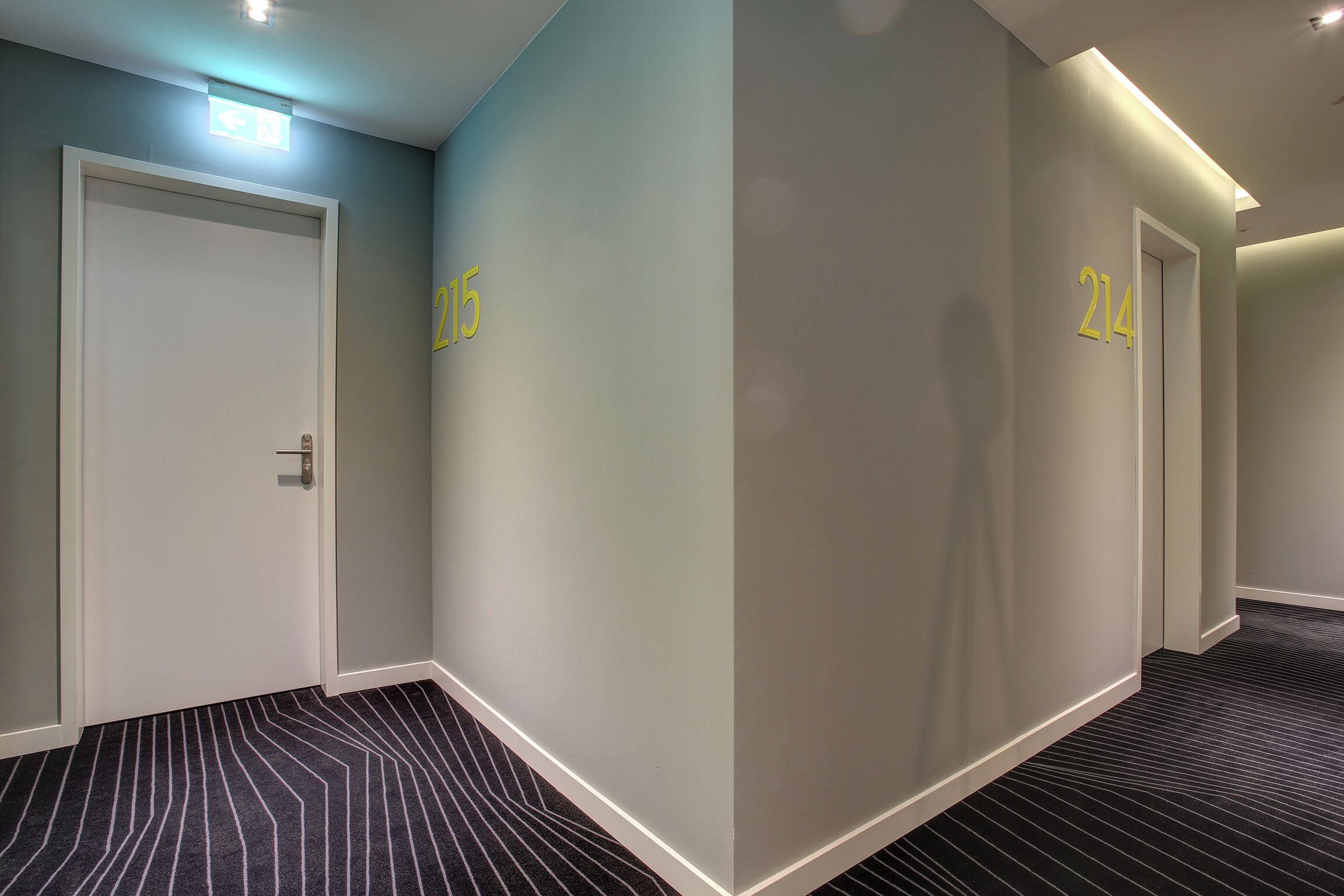 Un pasillo con puertas numeradas 215 y 214, pisos alfombrados e iluminación empotrada.