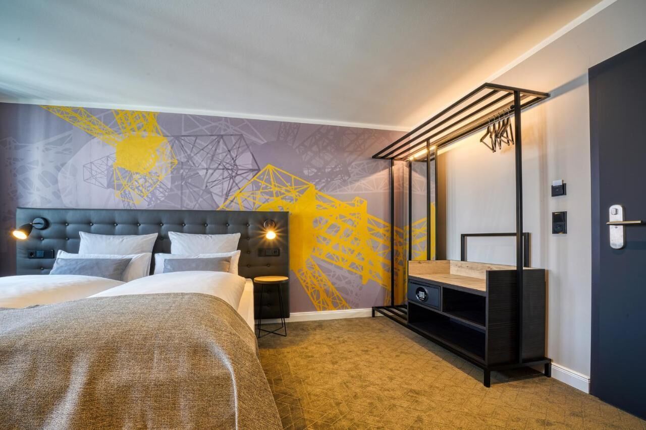Una camera d'albergo moderna con un grande letto, un comodino, una TV a parete e un armadio specchiato.