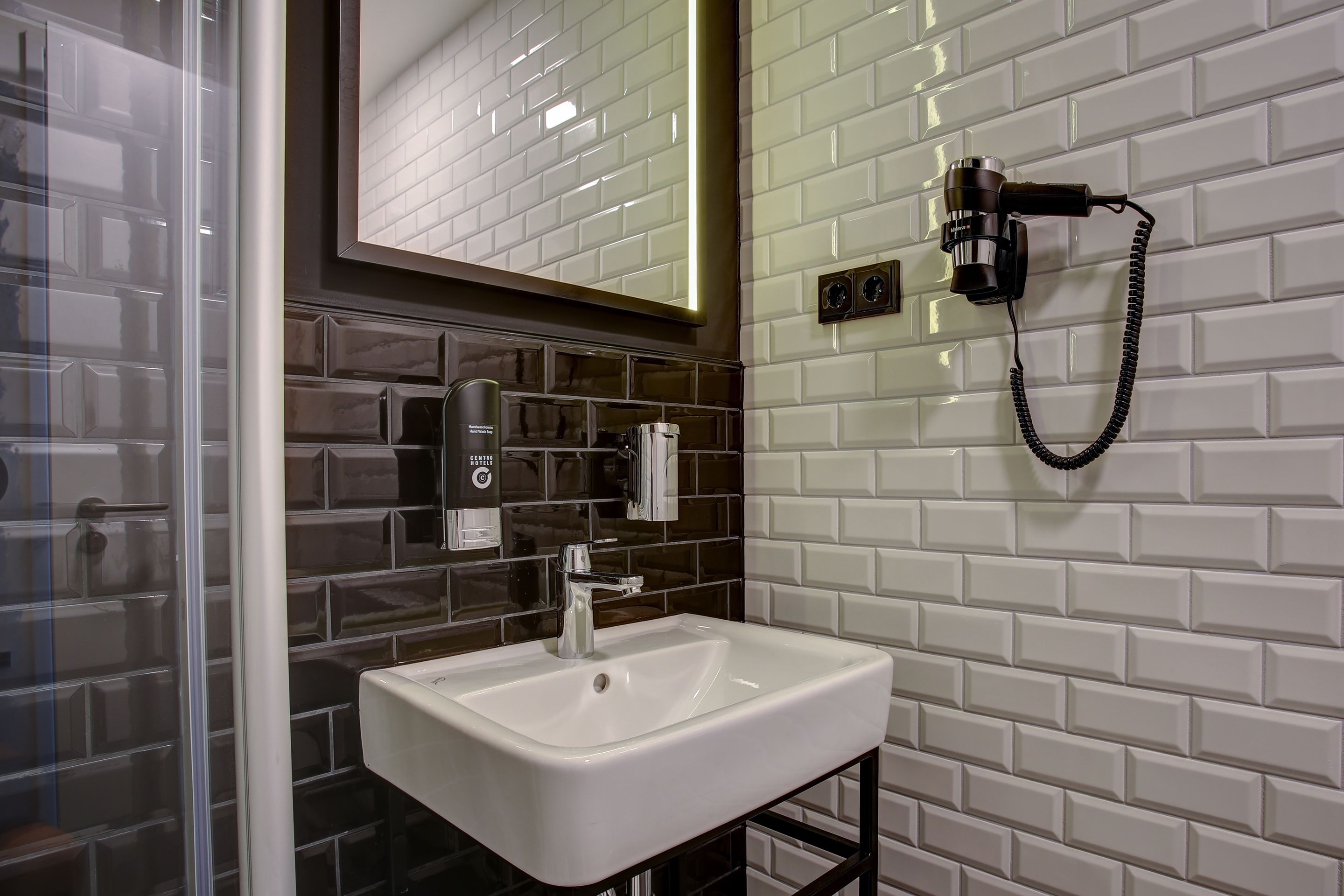 Un baño moderno con un lavamanos blanco, un espejo y un secador de pelo fijado a la pared.