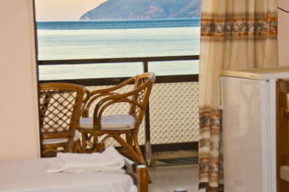 Un balcon avec deux lits, une chaise en osier et une vue sur la mer et une montagne.