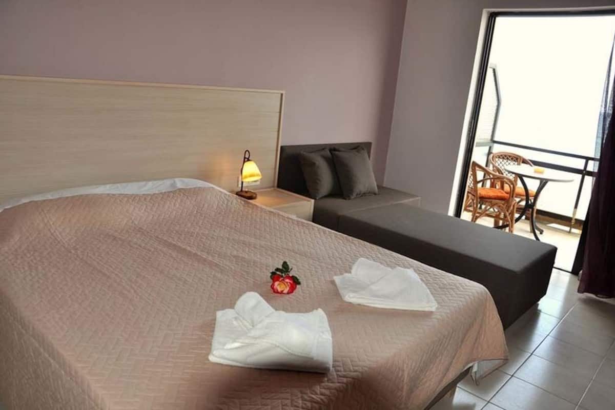 Une chambre d’hôtel avec un grand lit, un petit canapé, une table de chevet avec une lampe et un balcon doté de meubles en osier.