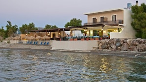 A waterfront property with a large building, outdoor seating area, and a stone wall. - Akrogiali (Kissamos)
