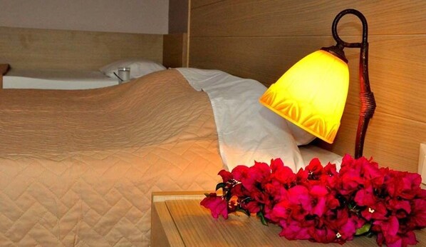 Una cama con una colcha acolchada, una lámpara de noche y un ramillete de flores rojas.