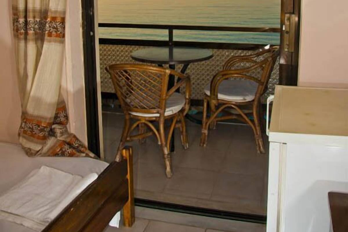 Un balcon avec vue sur la mer, des fauteuils en osier, une table et un lit.