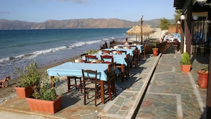 A seaside restaurant with outdoor seating overlooking the ocean, stone flooring, and potted plants. - Akrogiali (Kissamos)