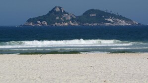 A beach with white sand and a rocky island in the background. - Tropical Barra Hotel (Rio de Janeiro)